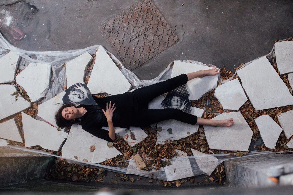 A woman dressed in black lies on Portland stones looking up at the sky
