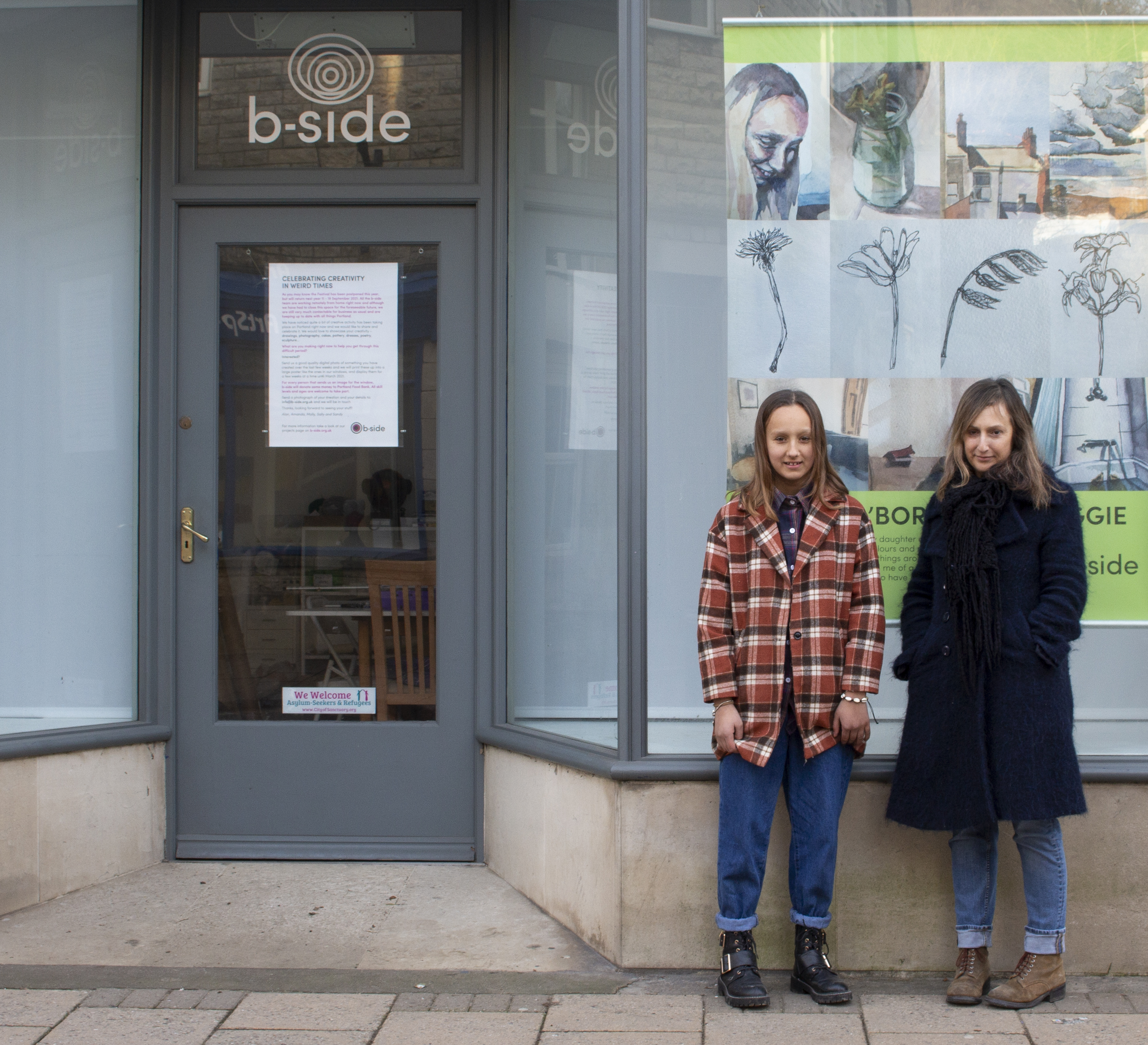 Two women stand in front of a shop window