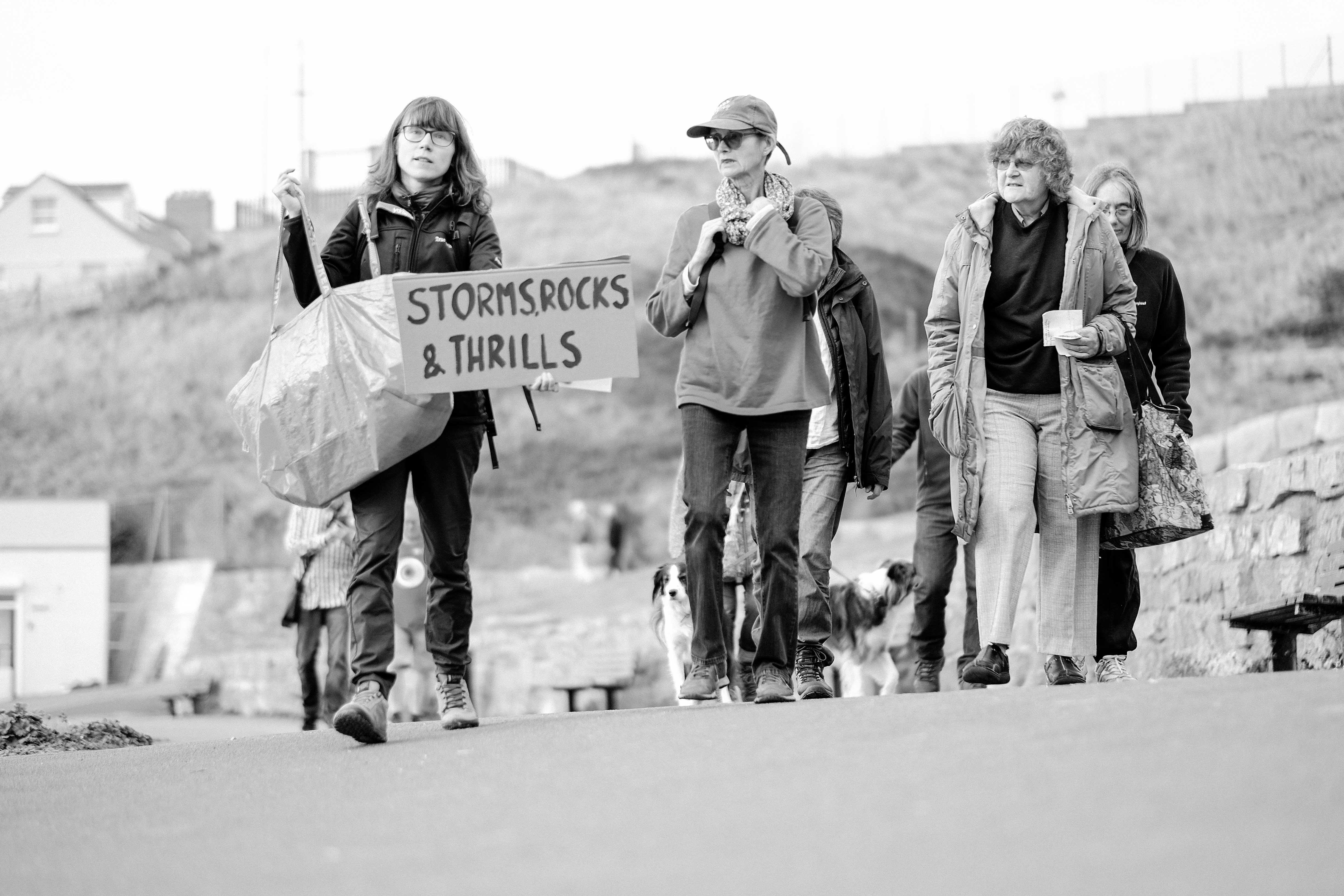 Woman leading a group with a sign reading 'Storms, Rocks and Thrills'