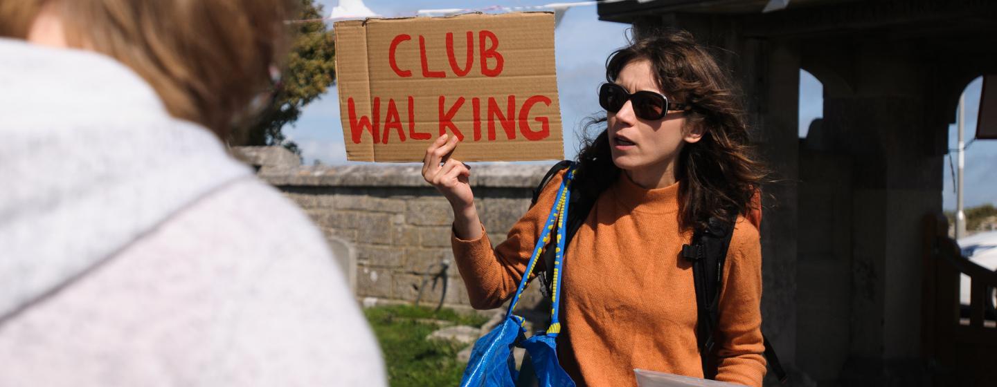 Woman holding up a 'club walking' sign