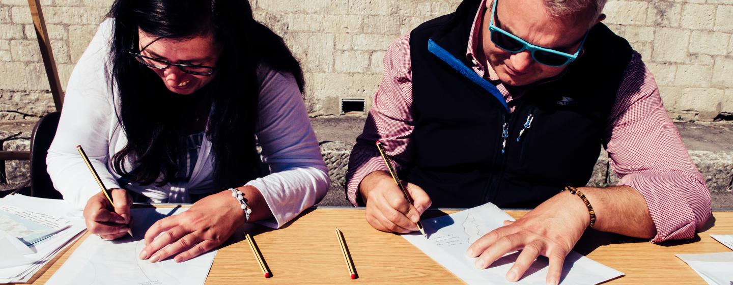 Two people sitting at a table with pencils and paper
