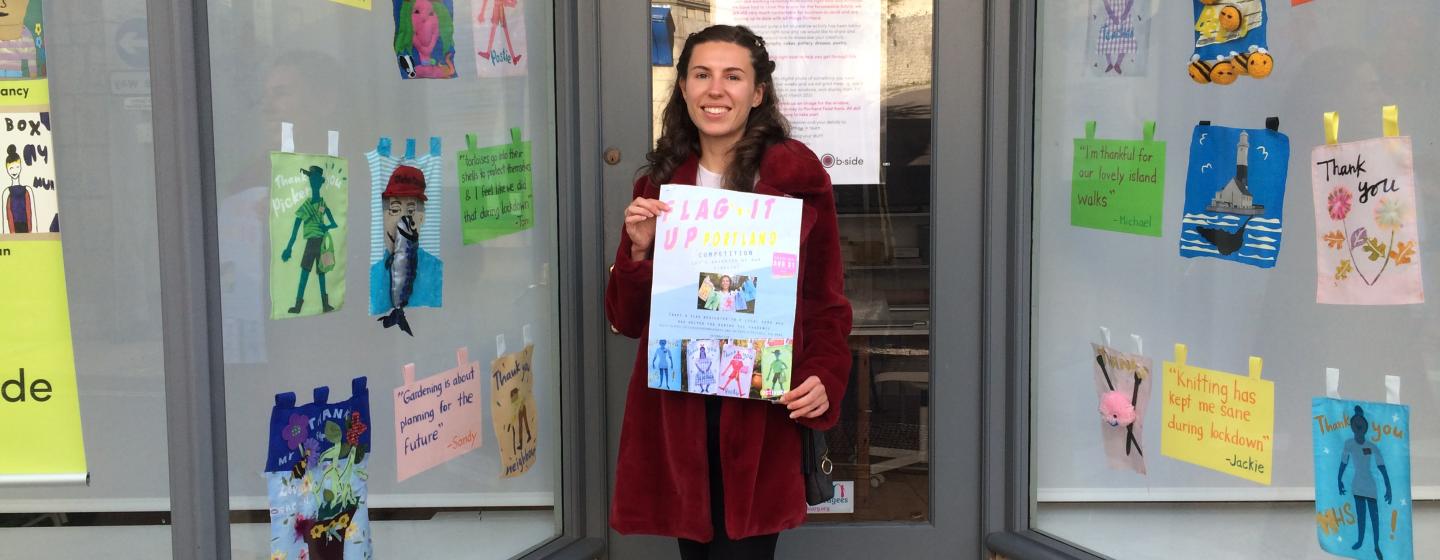 A young woman holding a poster standing outside a window