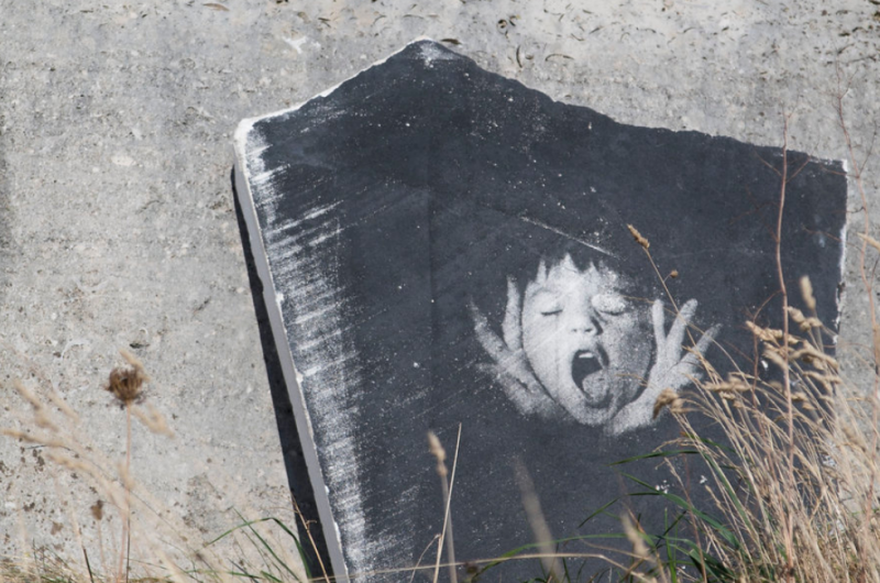 An image of a biys face screaming imprinted in black and white on the surface of a flat stone