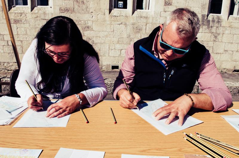 Two people sitting at a table with pencils and paper