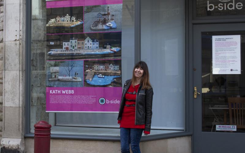 A photo of a woman laughing standing beside a large brightly coloured poster